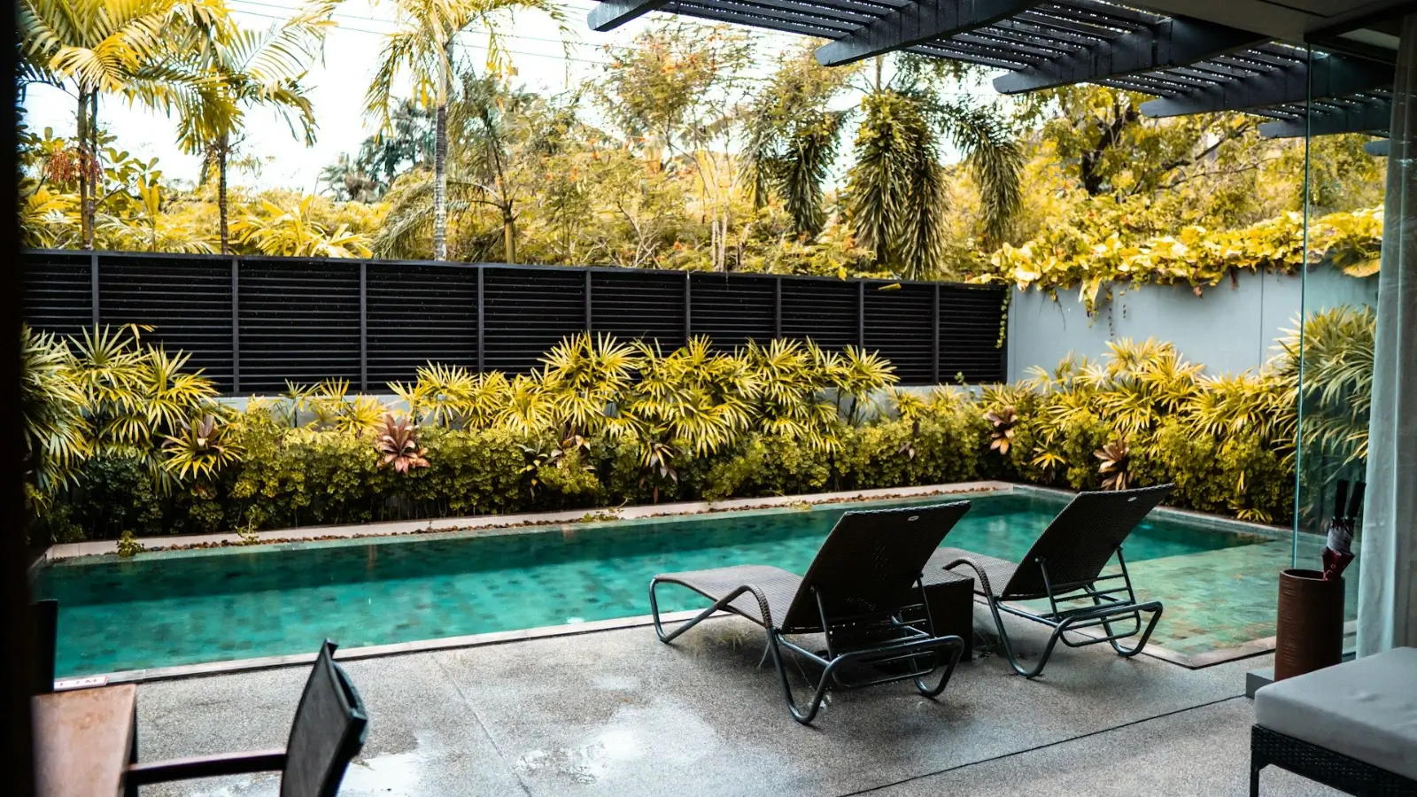 Modern backyard swimming pool surrounded by lounge chairs, greenery, and outdoor lighting