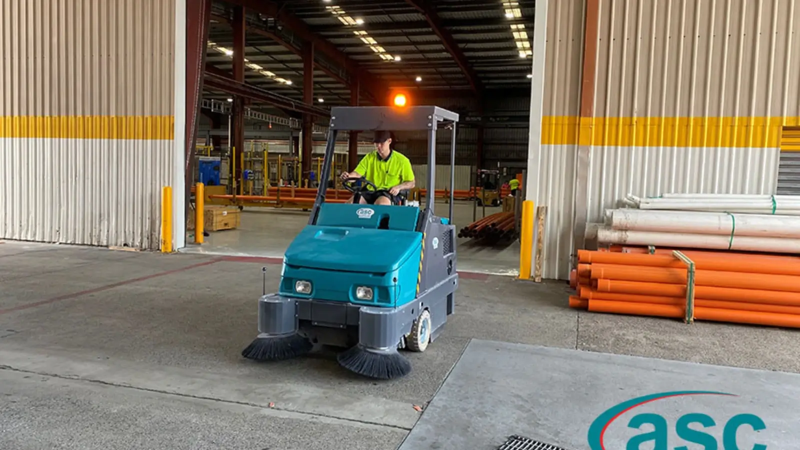 Operator using ride-on sweeper in a large industrial warehouse