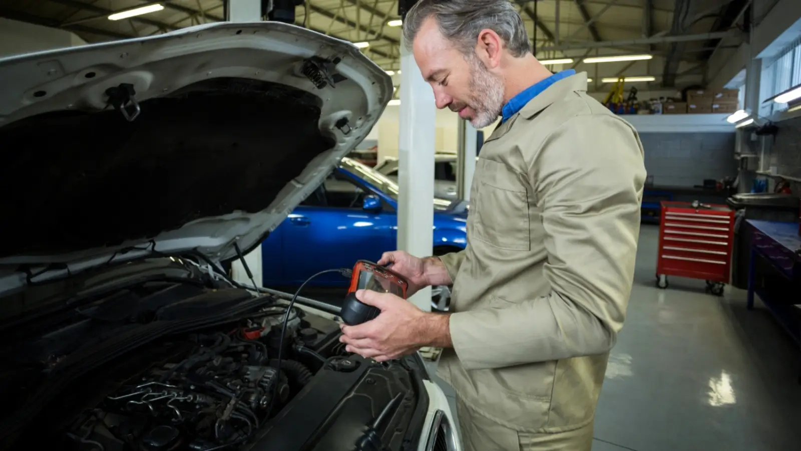 Mechanic checking a car alternator under the hood with a multimeter