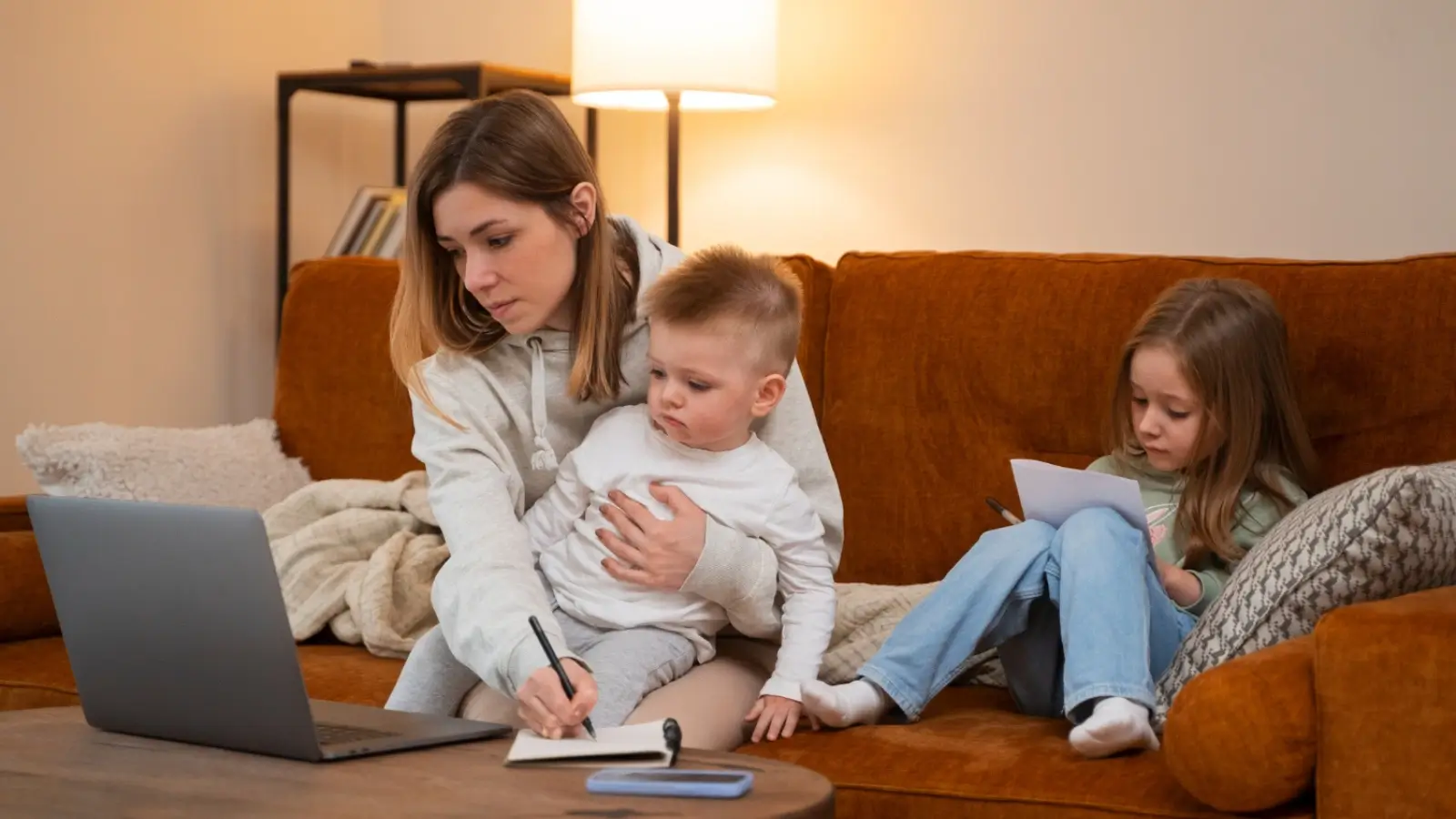 Parent working on a laptop at home while caring for children and managing side income