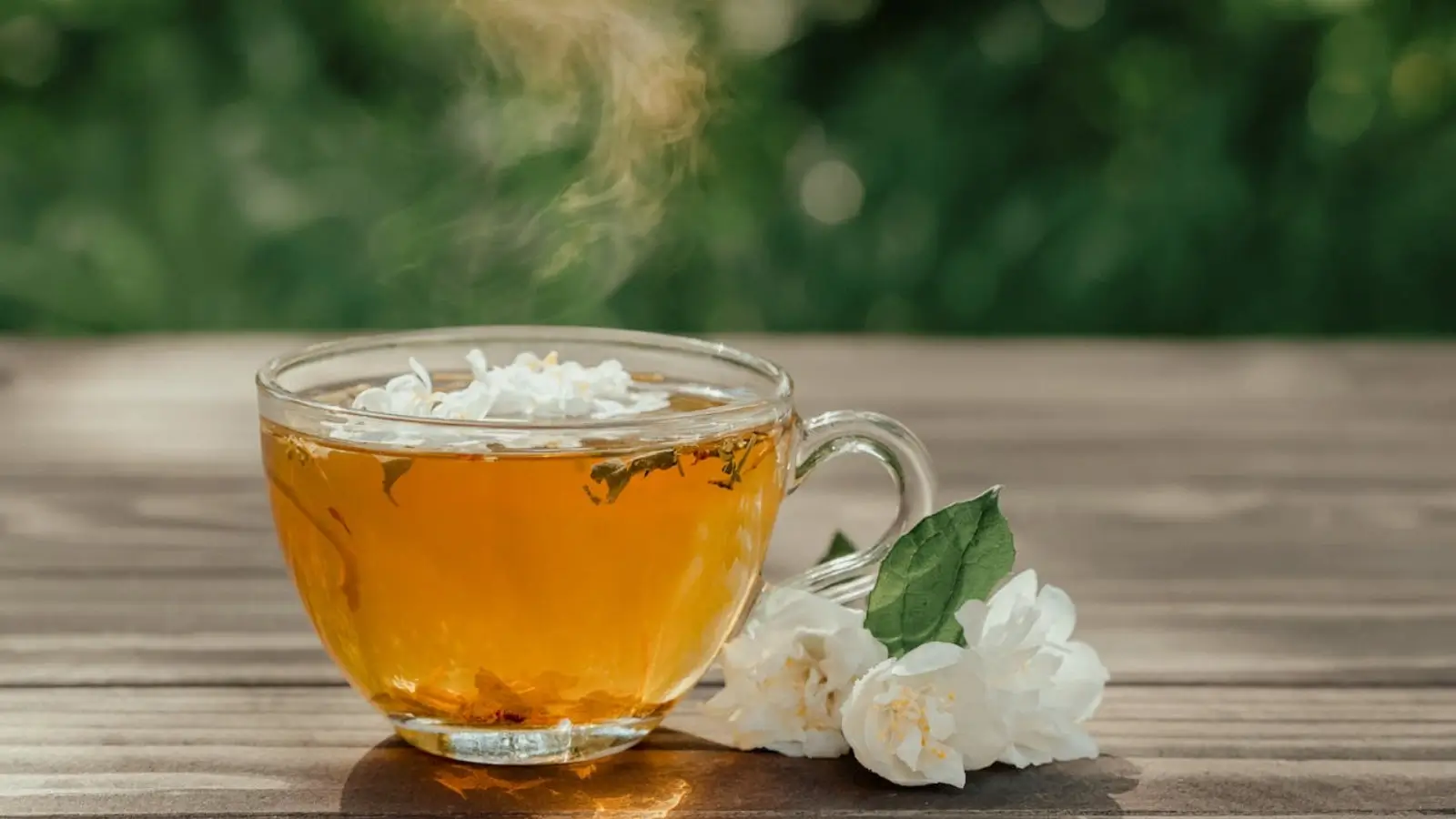 Steaming cup of jasmine tea with fresh jasmine flowers on a wooden table