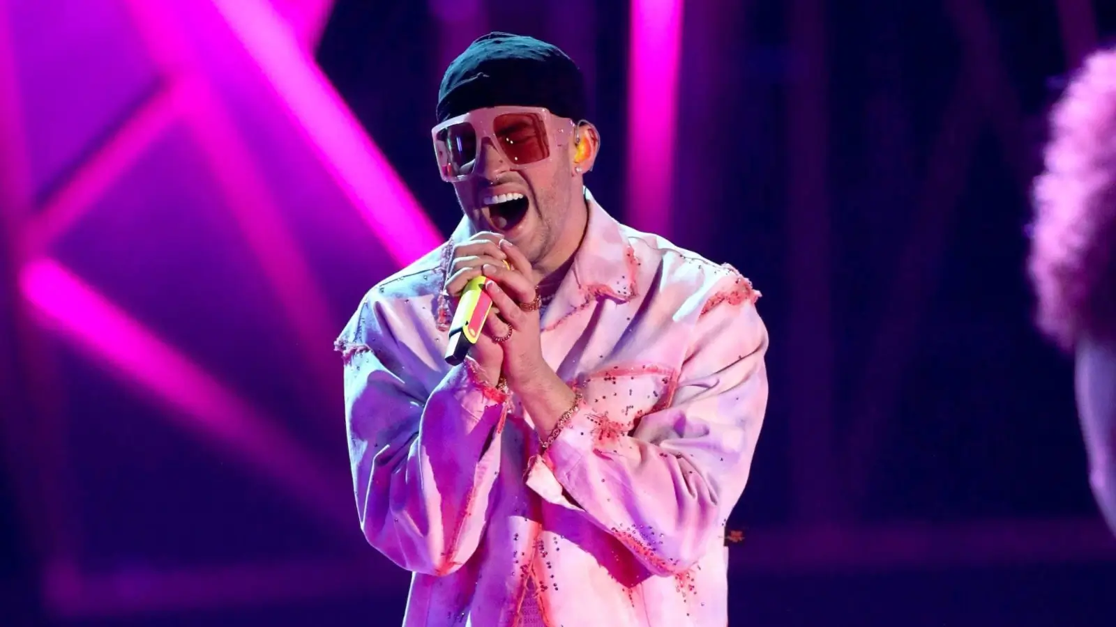 Bad Bunny performing on stage with vibrant lights and crowd cheering
