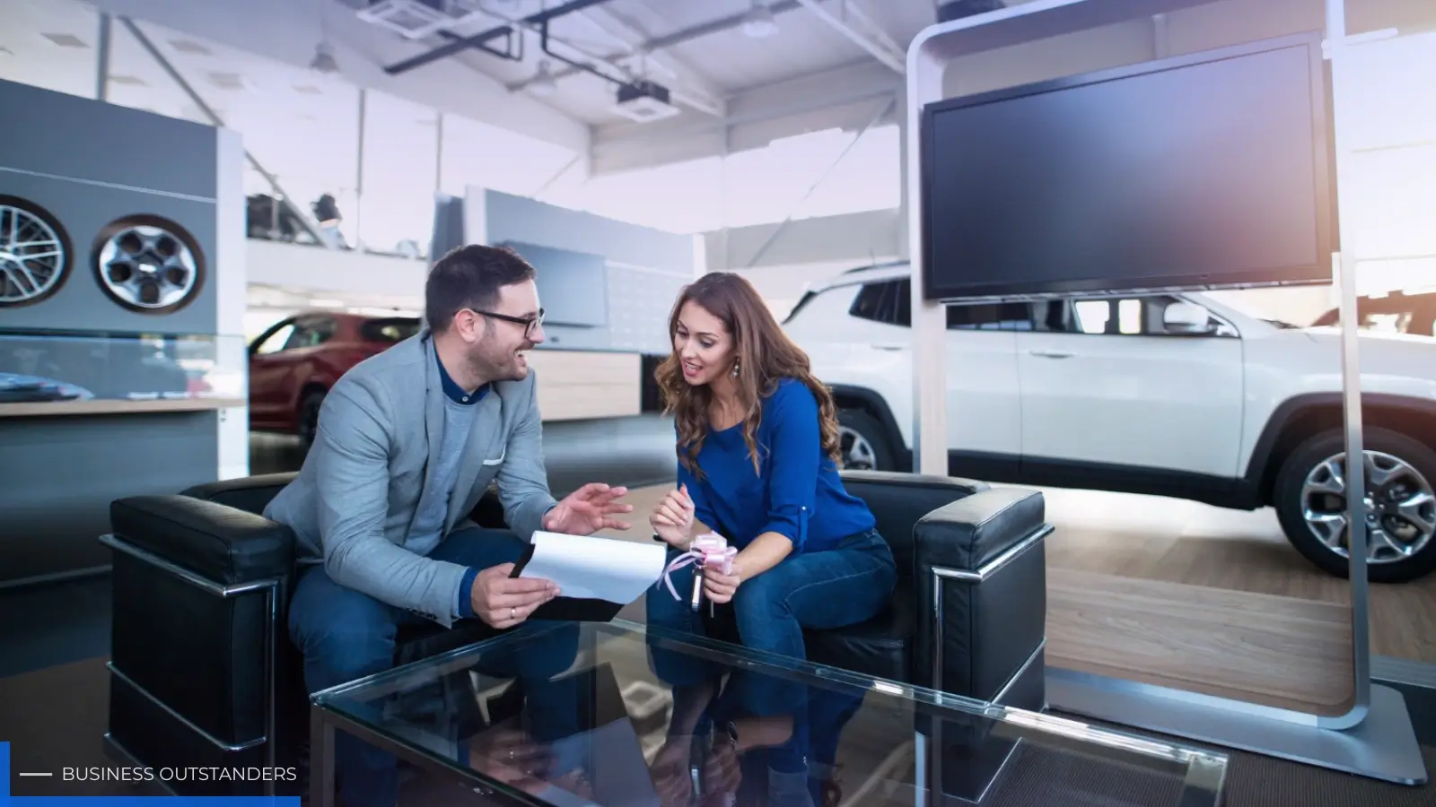 Car dealership salesperson helping a customer research vehicle options on a digital display